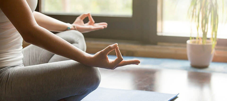 Attractive young woman working out at home, doing yoga exercise on blue mat, sitting in Easy Decent, Pleasant Posture , meditating, breathing, relaxing. Body close-up, focus on hand