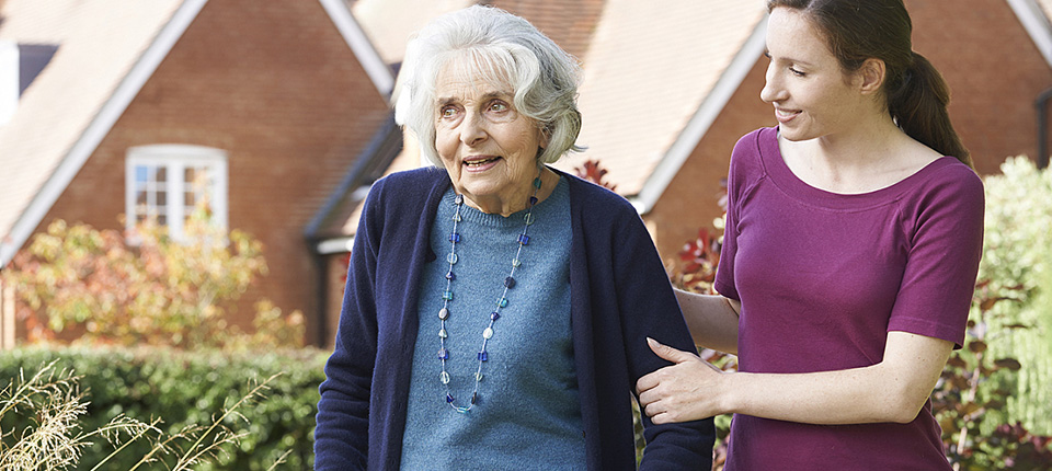 Daughter Helping Senior Mother To Use Walking Frame