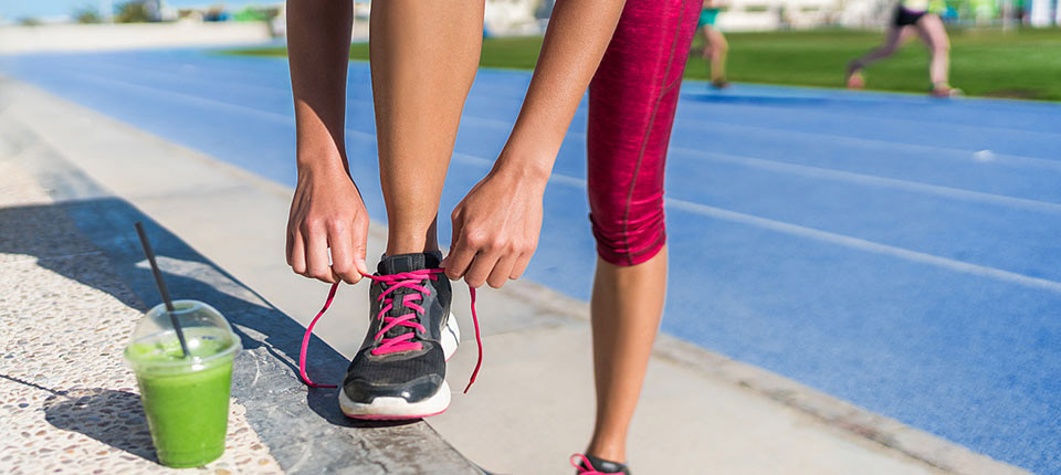 Healthy lifestyle woman runner tying running shoes drinking green smoothie cup juice drink before race workout on run tracks at outdoor stadium. Athlete getting ready for cardio training.; Shutterstock ID 640723678; PO: 123