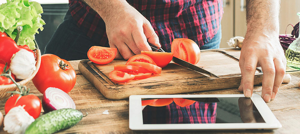 Man following recipe on digital tablet and cooking tasty and healthy food in kitchen at home on a sunny day